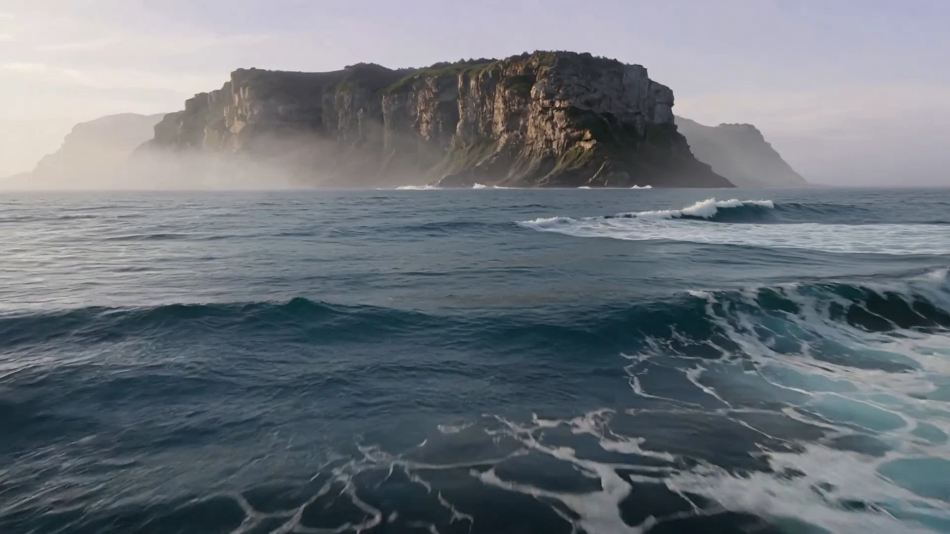Ocean waves below towering mist-covered coastal cliffs